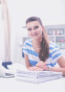 Elinde belgelerle masanın üstünde oturan gülümseyen kadın..