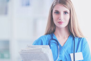 Hastane koridorunda steteskoplu kadın doktor portresi, elinde klasör var..