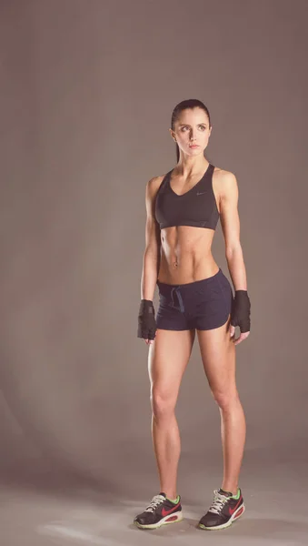 Muskulös ung kvinna poserar i sportkläder mot svart bakgrund. — Stockfoto