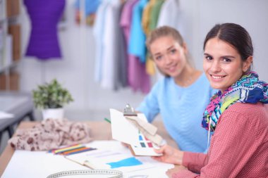 Güzel moda tasarımcısı stüdyoda masada oturuyor.