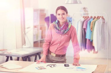 Güzel moda tasarımcısı stüdyoda masada oturuyor.
