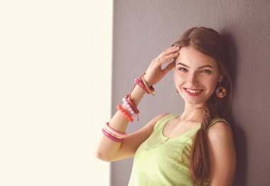 Gri duvarda gülümseyen genç bir kadının portresi.