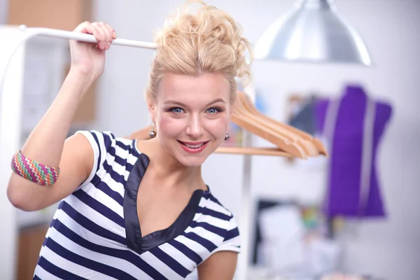 Mooie jonge stylist in de buurt van rack met hangers in office — Stockfoto