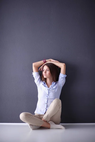 Portrait of a casual happy woman sitting on the floor on gray background — Stock Photo, Image