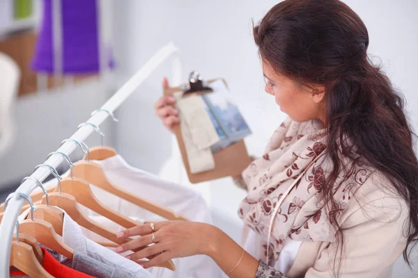 Mooie jonge stylist in de buurt van rack met hangers in office — Stockfoto