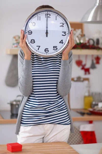 Happy young woman showing clock in christmas decorated kitchen — Stock Photo, Image