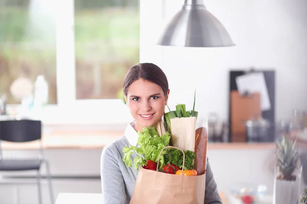 Young woman holding grocery shopping bag with vegetables . Standing in the kitchen — Stock Photo, Image