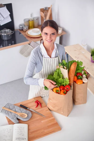 Een jonge vrouw die een boodschappentas met groenten vasthoudt. Staande in de keuken — Stockfoto