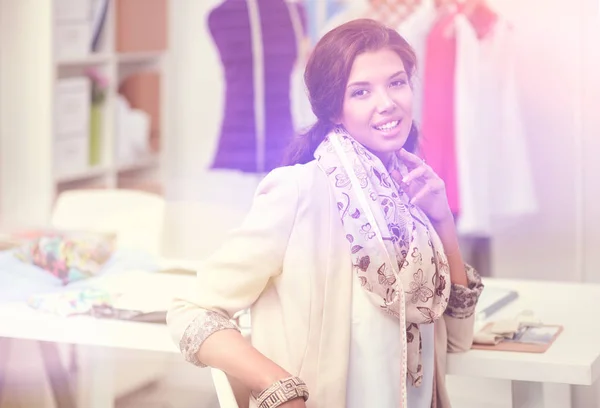 Beautiful young stylist near rack with hangers in office — Stock Photo, Image