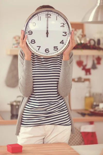 Happy young woman showing clock in christmas decorated kitchen