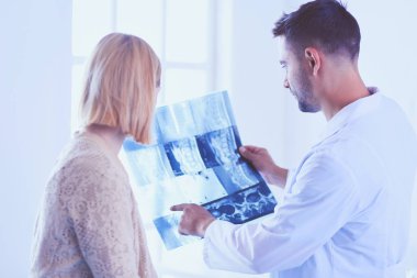 Yakışıklı doktor genç bayan hastasıyla konuşuyor ve ofisinde otururken notlar alıyor..