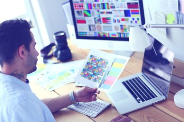 İnternette çalışırken bilgisayarın ve dizüstü bilgisayarın önünde grafik stüdyosunda oturan genç tasarımcının portresi.