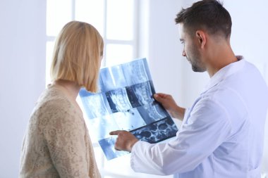 Yakışıklı doktor genç bayan hastasıyla konuşuyor ve ofisinde otururken notlar alıyor..