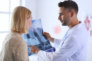 Yakışıklı doktor genç bayan hastasıyla konuşuyor ve ofisinde otururken notlar alıyor..