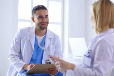 Yakışıklı doktor genç bayan doktorla konuşuyor ve ofisinde otururken notlar alıyor..