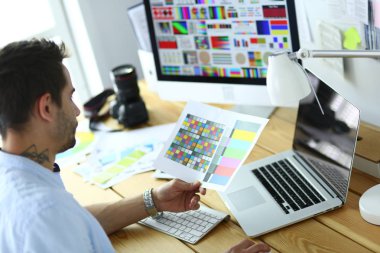 İnternette çalışırken bilgisayarın ve dizüstü bilgisayarın önünde grafik stüdyosunda oturan genç tasarımcının portresi.