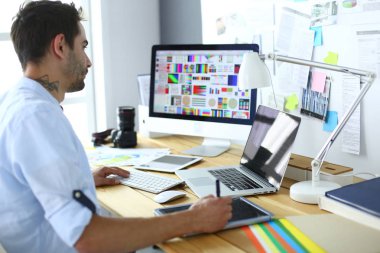 İnternette çalışırken bilgisayarın ve dizüstü bilgisayarın önünde grafik stüdyosunda oturan genç tasarımcının portresi.