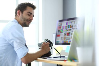 İnternette çalışırken bilgisayarın ve dizüstü bilgisayarın önünde grafik stüdyosunda oturan genç tasarımcının portresi.