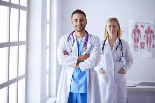 Handsome doctor is talking with young female doctor and making notes while sitting in his office. — Stock Photo, Image