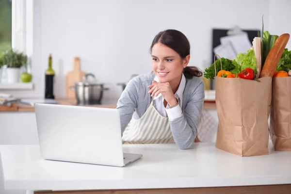 Lachende vrouw online winkelen met behulp van computer en creditcard in de keuken — Stockfoto