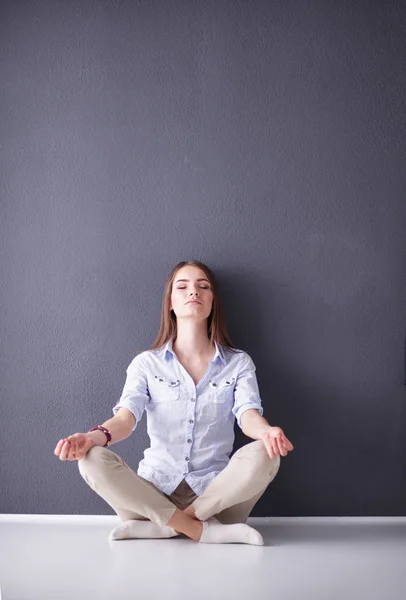 Portrait of a casual happy woman sitting on the floor on gray background — Stock Photo, Image