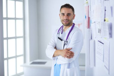 Genç ve kendinden emin erkek doktor portresi tıp ofisinde duruyor..