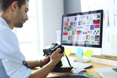 İnternette çalışırken bilgisayarın ve dizüstü bilgisayarın önünde grafik stüdyosunda oturan genç tasarımcının portresi.