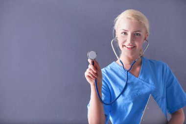 Steteskopla dinleyen kadın doktor, gri arka planda izole edilmiş.