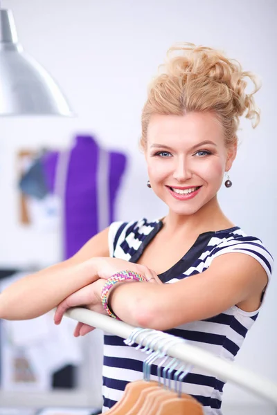 Mooie jonge stylist in de buurt van rack met hangers in office — Stockfoto