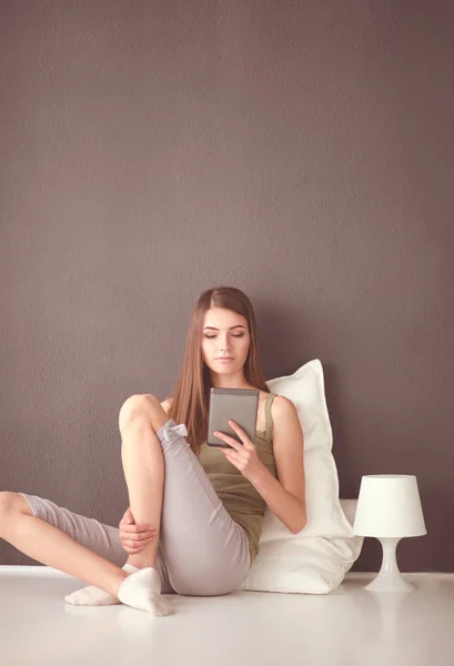 Mulher morena bonita sentada no chão com uma almofada e mesa plana — Fotografia de Stock