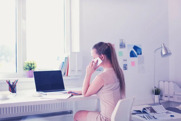 Jonge zakenvrouw zit aan het bureau en praat over de telefoon — Stockfoto