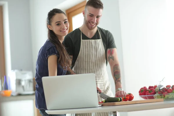 Молодий чоловік ріже овочі і жінка, що стоїть з ноутбуком на кухні — стокове фото