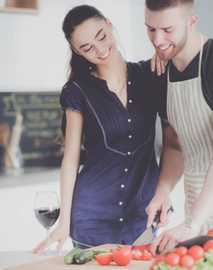 Sebze doğrayan genç bir adam ve mutfakta dizüstü bilgisayarı olan bir kadın.