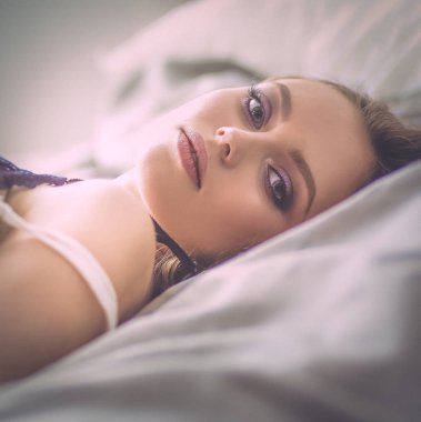 Güzel genç bir kadın beyaz yatakta yatıyor.
