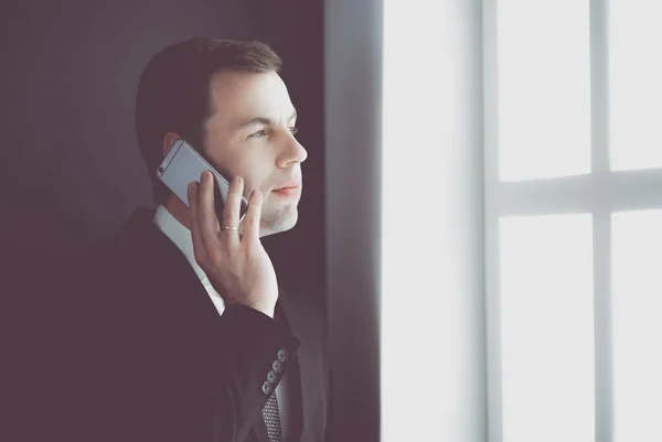 Handsome businessman talking on mobile phone in modern office. — Stock Photo, Image