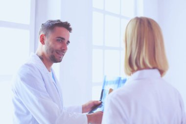 Yakışıklı doktor genç bayan doktorla konuşuyor ve ofisinde otururken notlar alıyor..