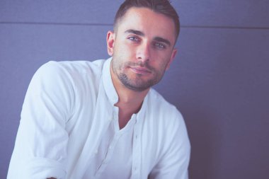 Gri arka planda yalnız oturan genç iş adamı.