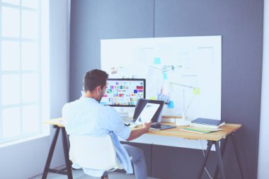 İnternette çalışırken bilgisayarın ve dizüstü bilgisayarın önünde grafik stüdyosunda oturan genç tasarımcının portresi.