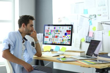 İnternette çalışırken bilgisayarın ve dizüstü bilgisayarın önünde grafik stüdyosunda oturan genç tasarımcının portresi.