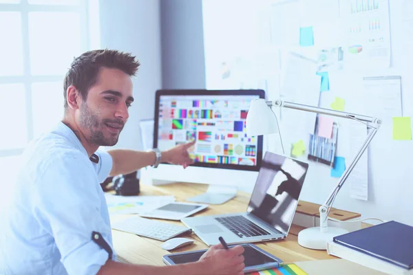 Retrato del joven diseñador sentado en el estudio gráfico frente a la computadora portátil y el ordenador mientras trabaja en línea. — Foto de Stock