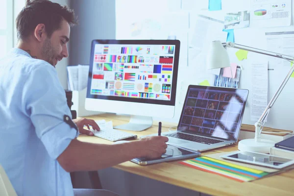 İnternette çalışırken bilgisayarın ve dizüstü bilgisayarın önünde grafik stüdyosunda oturan genç tasarımcının portresi.