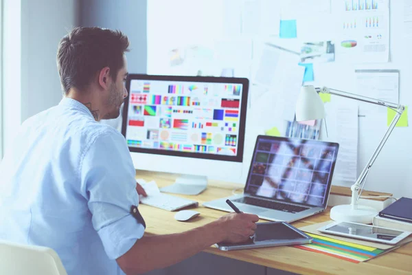 İnternette çalışırken bilgisayarın ve dizüstü bilgisayarın önünde grafik stüdyosunda oturan genç tasarımcının portresi.