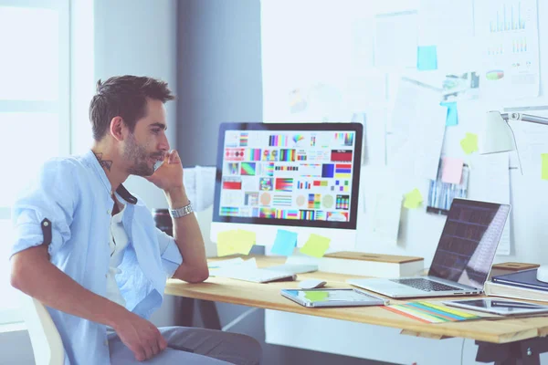 İnternette çalışırken bilgisayarın ve dizüstü bilgisayarın önünde grafik stüdyosunda oturan genç tasarımcının portresi.