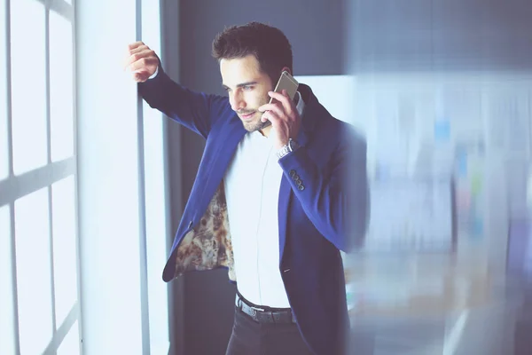 Homem de negócios de terno falando ao telefone e olhando para longe perto da janela . — Fotografia de Stock