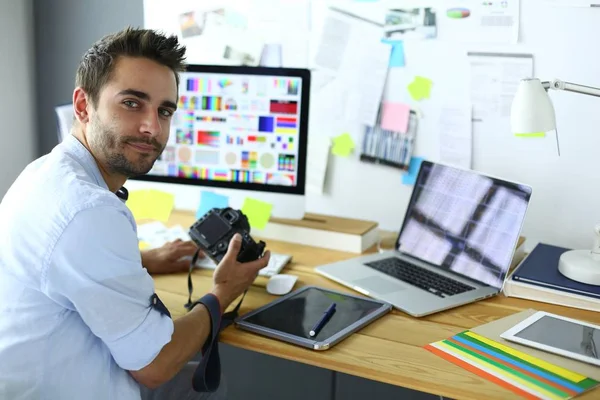 Portrait of young designer sitting at graphic studio in front of laptop and computer while working online.