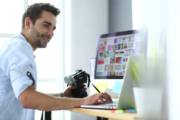 Retrato del joven diseñador sentado en el estudio gráfico frente a la computadora portátil y el ordenador mientras trabaja en línea. — Foto de Stock