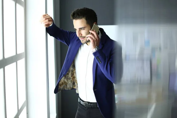 Affärsman i kostym prata telefon och tittar bort nära fönstret. — Stockfoto