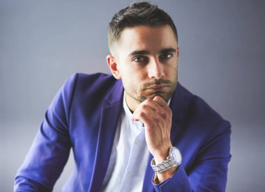 Gri arka planda yalnız oturan genç iş adamı.