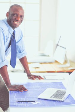Ofiste bilgisayar ve planlarla çalışan Afrikalı Amerikalı bir mimar.