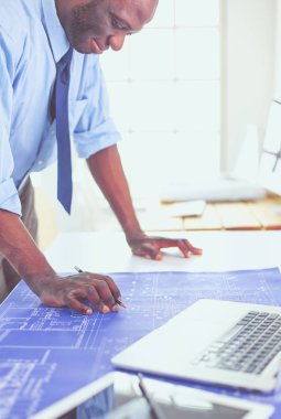 Ofiste bilgisayar ve planlarla çalışan Afrikalı Amerikalı bir mimar.